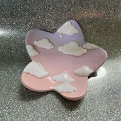 a pink, purple and white plate with clouds on it sitting on a silver surface