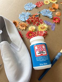 a pair of white shoes sitting next to a bottle of glue and some paper flowers