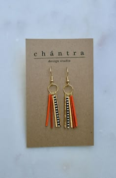 the earrings are orange, black and white with gold details on them in front of a card