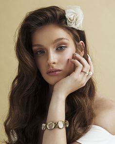 a woman with long brown hair wearing a white flower in her hair and bracelet on her wrist