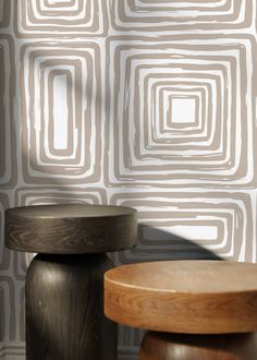 two stools in front of a wall with an abstract pattern on it and a wooden table