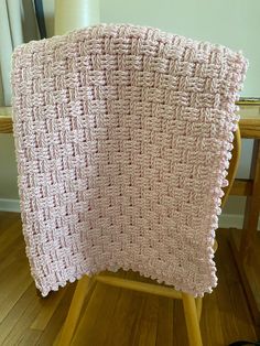 a pink crocheted blanket sitting on top of a wooden chair