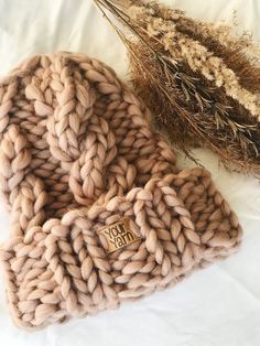 two knitted beanies sitting on top of a white bed next to dried plants