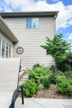 a house with a clock on the side of it's wall next to some plants