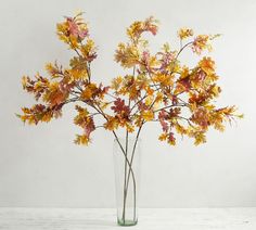 a vase filled with yellow and red flowers on top of a wooden table next to a white wall