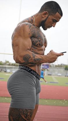 a man with tattoos on his arms and legs is looking at his cell phone while standing on a track