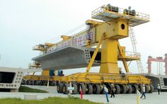 a large crane is parked in front of a building and people are walking around it