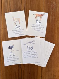 four cards with animals and letters on them sitting on a wooden table next to each other