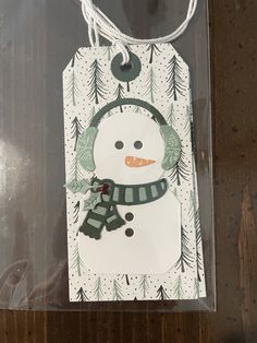 a snowman with a green hat and scarf on it's head hanging from a string