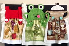 three towels are hanging on the wall next to cups and teapots, one has a green frog