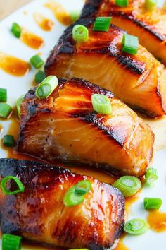 three pieces of salmon on a plate with green onions