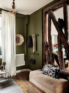 a living room with green walls and wooden furniture in front of a large mirror on the wall