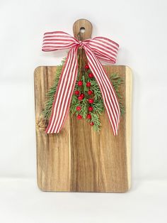 a wooden cutting board with a red and white bow on it, hanging from the side