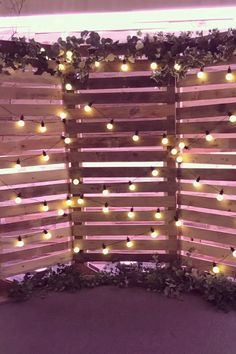 a wooden fence with lights on it and some plants growing around the top half of it