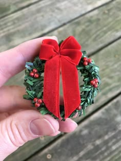 a hand holding a christmas wreath ornament with a red bow and holly berries