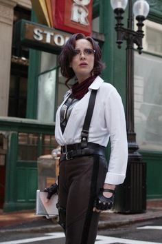 a woman standing on the street with her hands in her pockets and wearing suspenders