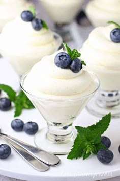 three desserts with blueberries and whipped cream in small glass dishes on a table