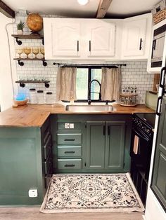 a kitchen with green cabinets and white walls, an area rug on the floor in front of the sink