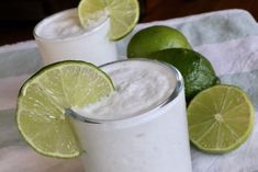 two glasses filled with milk and limes on top of a towel next to each other