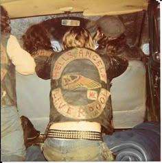 two people in the back of a truck with their backs turned to the camera, and one person wearing a leather jacket