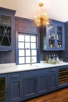 a kitchen with blue cabinets and white counter tops, gold chandelier above the sink