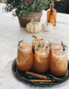 four jars filled with liquid sitting on top of a table next to cinnamon sticks and pumpkins