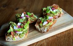 three pieces of bread topped with guacamole and onions on a wooden cutting board