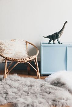 a toy dinosaur standing on top of a wooden chair next to a rug and cabinet