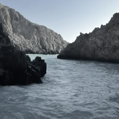 the water is crystal blue and there are mountains in the background with rocks on either side