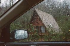 rain is falling on the windshield of a car as it sits in front of a cabin