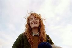 a woman with red hair is smiling and looking up at the sky while wearing a green sweater