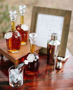 three bottles of liquor on a table with ice cubes and a sign in the background