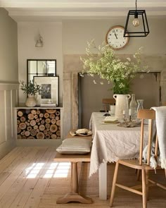 a dining room table with chairs and a clock on the wall above it, in front of a fireplace