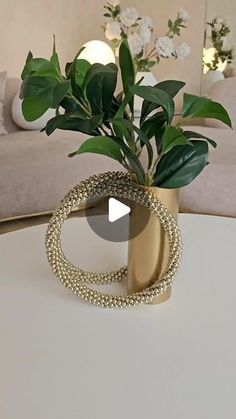 a plant in a gold vase sitting on a white table next to a beige couch