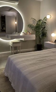 a white bed sitting under a round mirror in a bedroom next to a table with a plant