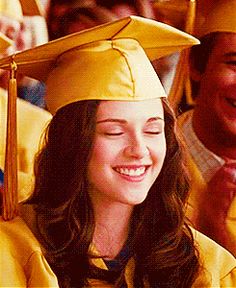 a woman in a graduation cap and gown smiles as she sits with other people behind her