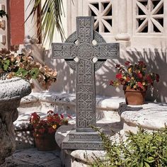 a cross sitting on the ground next to potted plants