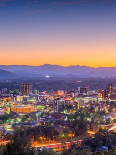 the city is lit up at night with mountains in the background