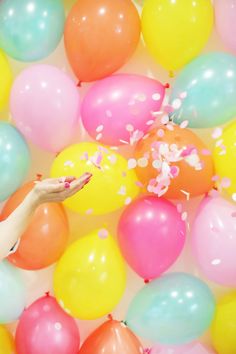 a woman is reaching for some confetti in a pool of balloons