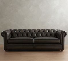 a black leather couch sitting on top of a hard wood floor next to a wall