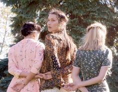 three women standing next to each other with trees in the background