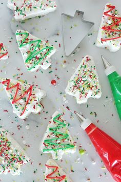 white frosted christmas tree cookies with sprinkles and green plastic bottle next to them