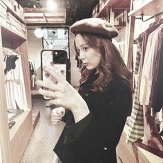 a woman taking a selfie with her phone in a clothing store while wearing a hat