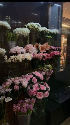 many different types of flowers in vases on display behind a glass window at a flower shop