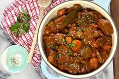 a pot filled with meat and vegetables on top of a table next to a wooden spoon