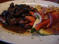 a white plate topped with meat and veggies on top of a wooden table