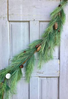 pine cones and fir needles hang from the side of a wooden door with white ornaments on it