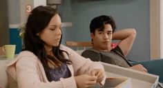 a man and woman sitting on a couch looking at something in a box that they are holding