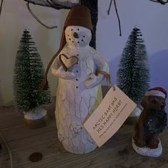 a ceramic snowman holding a sign next to a small bear on a table with pine trees