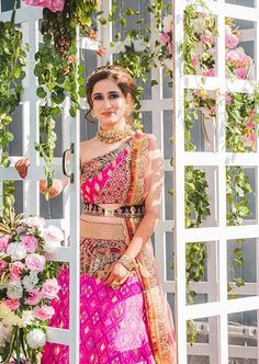 a woman in a pink and gold outfit standing next to a flower covered wall with flowers on it